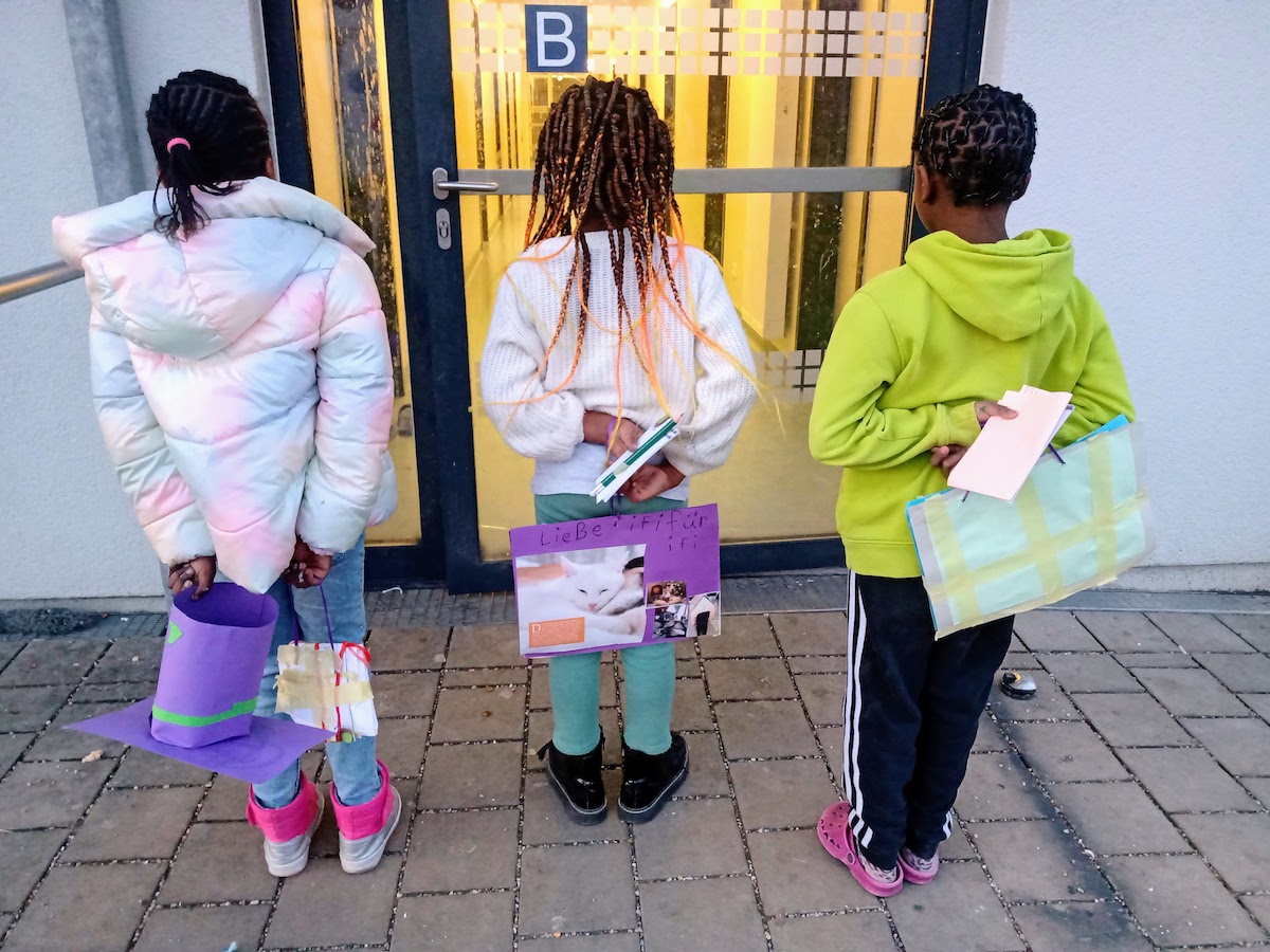 3 Kinder halten kleine Kunstwerke, die sie gebastelt haben, hinter dem Rücken